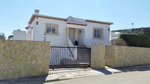 A two-story house with a tiled roof, a gated entrance, and a stone wall.
