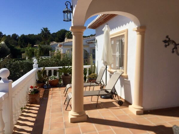 A balcony with a white railing, potted plants, a white umbrella, and a chair.