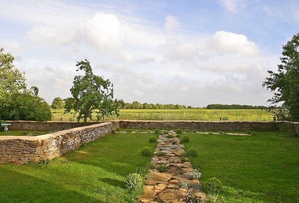 A stone pathway leading through a grassy area with stone walls on either side, surrounded by trees and fields.