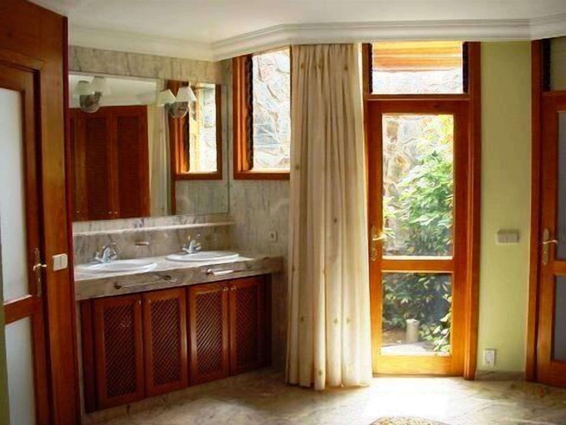 A bathroom with wooden cabinets, a marble countertop, and a window with curtains.