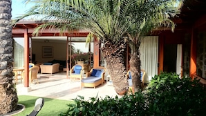 A covered outdoor seating area with wicker furniture and a palm tree.