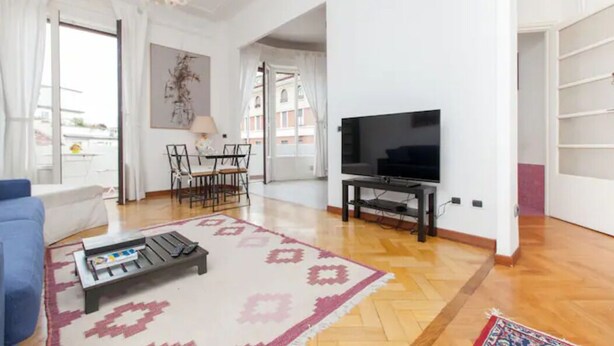 A living room with a TV, a sofa, a dining table with chairs, and a chandelier. - Petrella (Milano)