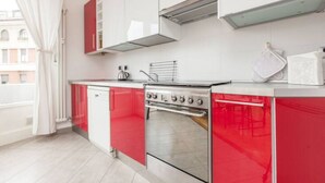 A modern kitchen with red and white cabinetry, a stainless steel stove, and a window with curtains. - Petrella (Milano)