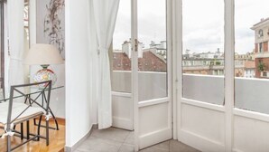 A balcony with a city view, a table with a lamp, and a chair. - Petrella (Milano)