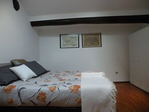Un dormitorio con una cama, almohadas, una colcha y dos mapas enmarcados en la pared.