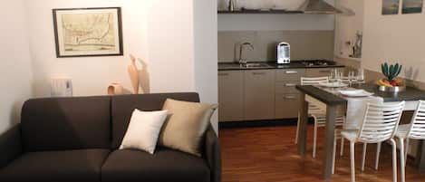Un espace de vie compact comprenant un canapé, une table à manger avec des chaises, un coin cuisine et une carte encadrée accrochée au mur.