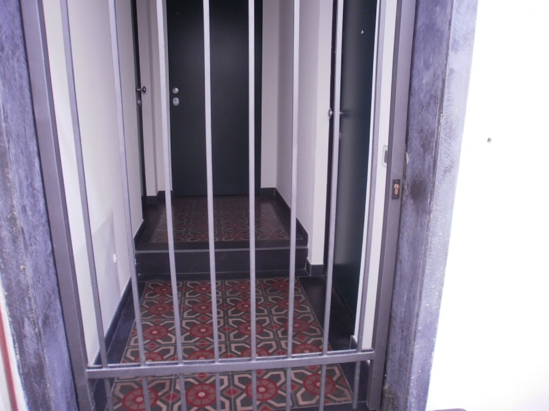 Eine enge Treppe mit einem gemusterten Boden führt zu einer Tür.