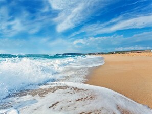 A beach with waves crashing onto the shore, a clear sky, and distant buildings.