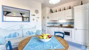 Una cocina moderna con armarios blancos, una mesa de comedor con mantel estampado azul y un bol de fruta.