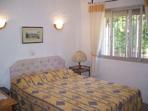 A bedroom with a bed, a lamp, a picture on the wall, and a window with curtains.