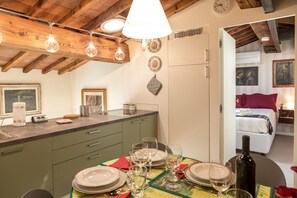 A dining area with a table set for four, a bottle of wine, and a kitchen with a clock on the wall.