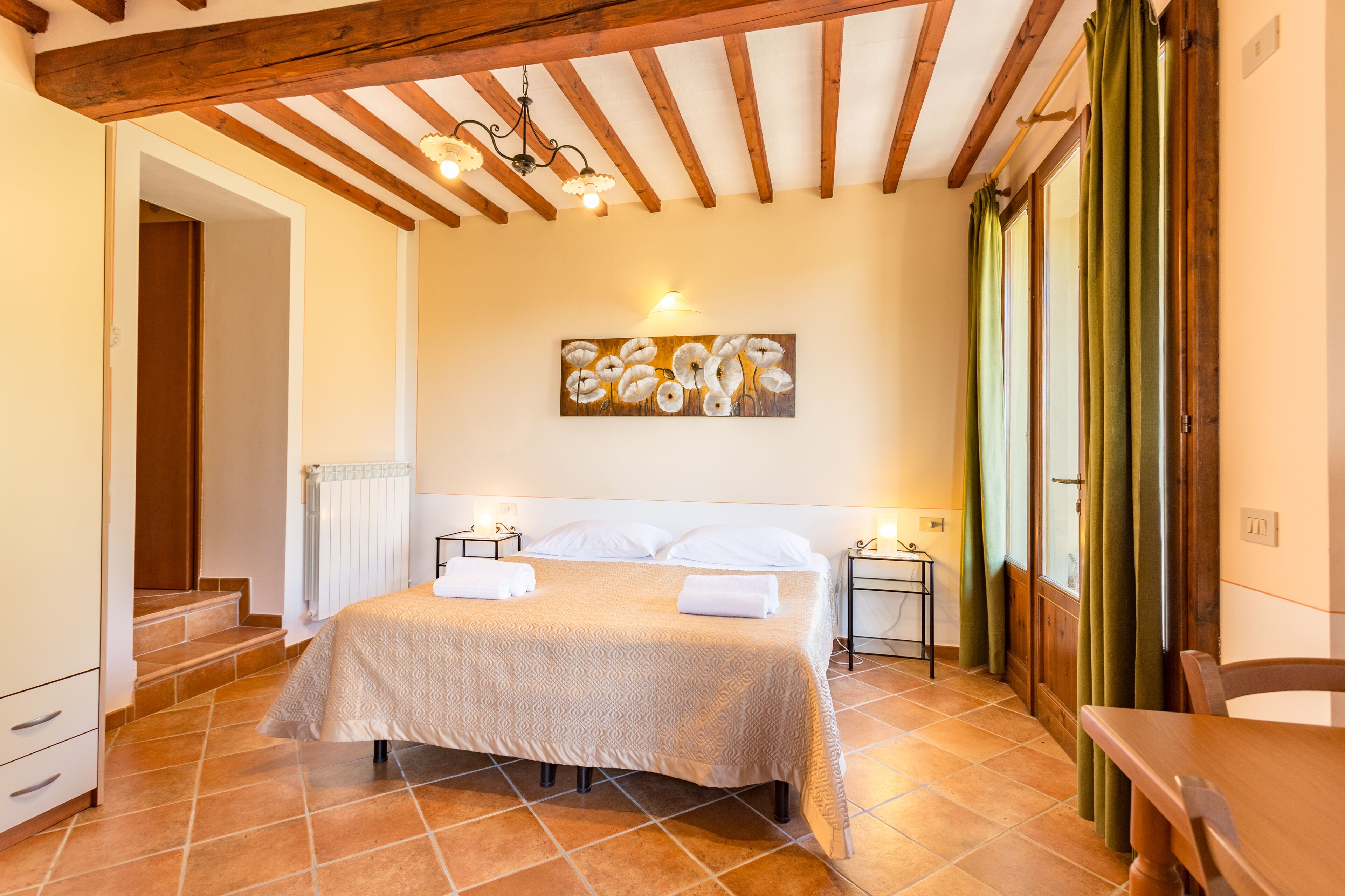 A bedroom with a bed, a painting, a nightstand, and a chair.