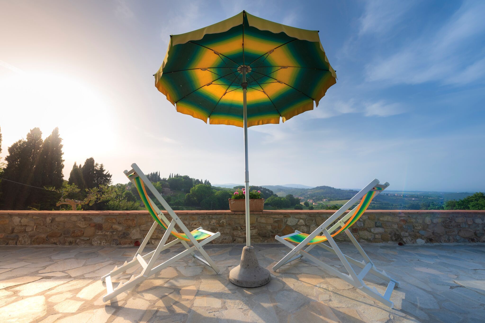 Pátio com duas cadeiras de descanso e um grande guarda-sol, com vista para uma paisagem deslumbrante.