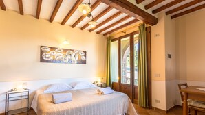 Un dormitorio con una cama grande, una mesita de noche, un cuadro y vistas al exterior a través de una puerta.