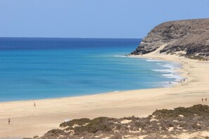 A beach with clear blue waters, sandy shore, and rocky cliffs.