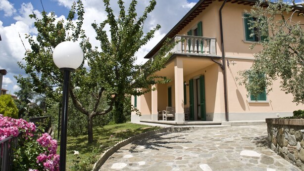 Una casa de dos pisos con un sendero de piedra que conduce a la entrada, rodeada de vegetación y un cielo despejado.