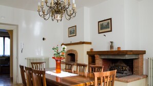 Un comedor con una mesa y sillas de madera, un candelabro, una chimenea y cuadros en la pared.