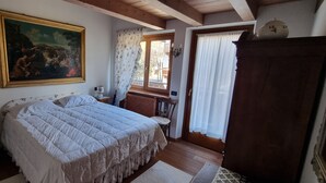 Een slaapkamer met een groot bed, een houten dressoir, een schilderij aan de muur en een raam met gordijnen.