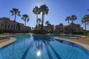 Una piscina cristallina circondata da palme e un edificio a più piani con balconi.
