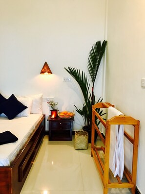 A small, neatly arranged bedroom with a bed, bedside table, lamp, and potted plants. - Cozy Bay (Arugam Bay)