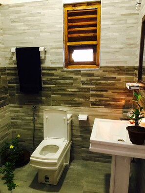 A bathroom with a toilet, sink, and a window with a wooden blind. - Cozy Bay (Arugam Bay)