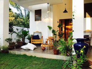 A covered outdoor seating area with a wooden bench, potted plants, and a large vase. - Cozy Bay (Arugam Bay)