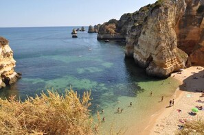 A coastal beach with clear waters, rocky cliffs, and people enjoying the beach and water.