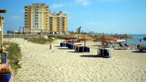 A beach with sun loungers, umbrellas, and a large hotel in the background. - Beautiful, double BEACH FRONT Penthouse, Breathtaking View, Wi-Fi, SAT TV, Pool (San Javier)