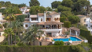 Uma grande villa com piscina, várias varandas e vegetação exuberante.