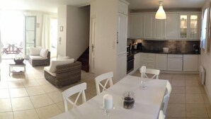 A bright living room with a sofa, a dining table with chairs, and a kitchen area with cabinets and a clock. - House / Villa - Saint-Rémy-de-Provence (Saint-Rémy-De-Provence)
