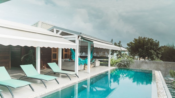 Ein moderner Poolbereich im Freien mit Liegestühlen, einer überdachten Sitzgelegenheit und Blick auf die umliegende Landschaft.