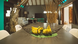 Ein Esstisch mit einem Drahtkorb, der Bananen enthält, einer grünen Tischmatte und einer Holzbalkendecke mit grüner Beleuchtung.