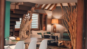 Ein modernes Wohnzimmer mit Essbereich, mit einem großen Baumstamm als Mittelpunkt, weißer Möbel und einer Lampe.