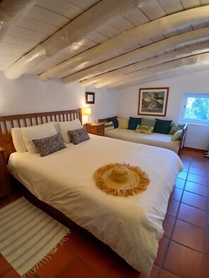 A bedroom with a large bed, a nightstand, a bedside table, a window, and a painting on the wall.