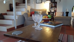 A living room with a wooden coffee table, two crystal glasses, a bowl of fruit, and a book.