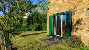 A stone building with a green door and window shutters, surrounded by a grassy yard and trees.