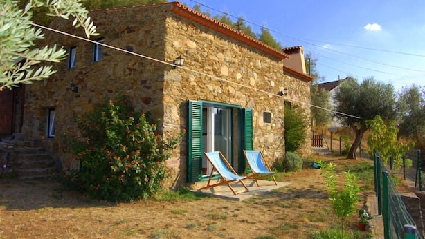 A stone building with a small porch, two chairs, and a garden.