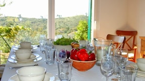 A table set for dining with bowls, glasses, and a bowl of red peppers, overlooking a hilly landscape.
