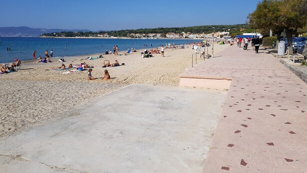 Une plage où l’on peut se prélasser au soleil et se baigner, un ciel dégagé et une promenade dallée.