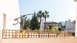 Un balcon avec une balustrade en bois, un lampadaire et, au fond, un bâtiment avec un toit recouvert de tuiles.