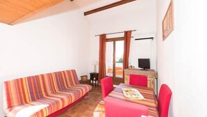 Une pièce chaleureuse avec un canapé à rayures, une table à manger entourée de chaises rouges et un téléviseur en arrière-plan.