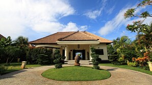 Una casa amb teulada de palla, un jardí ben cuidat i plantes tropicals.