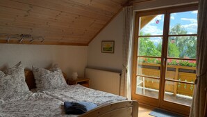 Een slaapkamer met een houten bed, een radiator, een raam met gordijnen en uitzicht op een tuin.