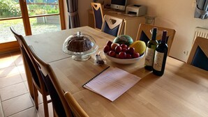 Een eettafel met taart, een schaal fruit en flessen wijn.