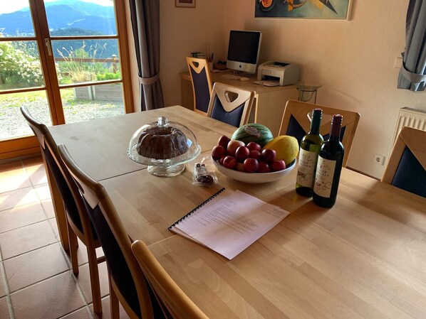 Una mesa de comedor con un pastel, un cuenco de fruta y botellas de vino.