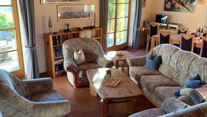 Een gezellige woonkamer met een open haard, houten balken en een eethoek met een tafel en stoelen.