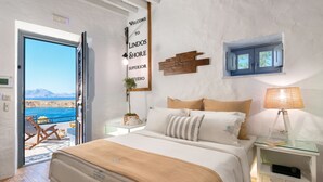 A bedroom with a bed, bedside tables, a nightstand, a wall-mounted sign, a window, and a view of the sea. - Brand New!!! Lindos shore Superior Studio just above Lindos main beach !!! (Rhodes)