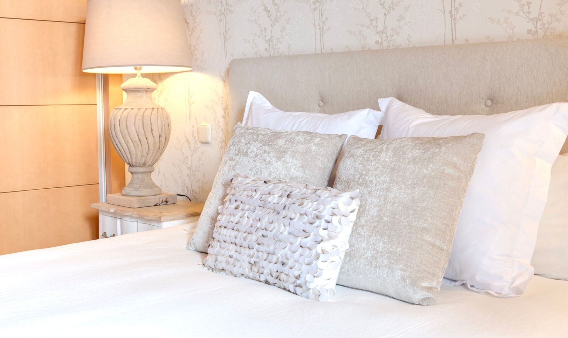Una cama bien hecha con varias almohadas y una lámpara de noche.