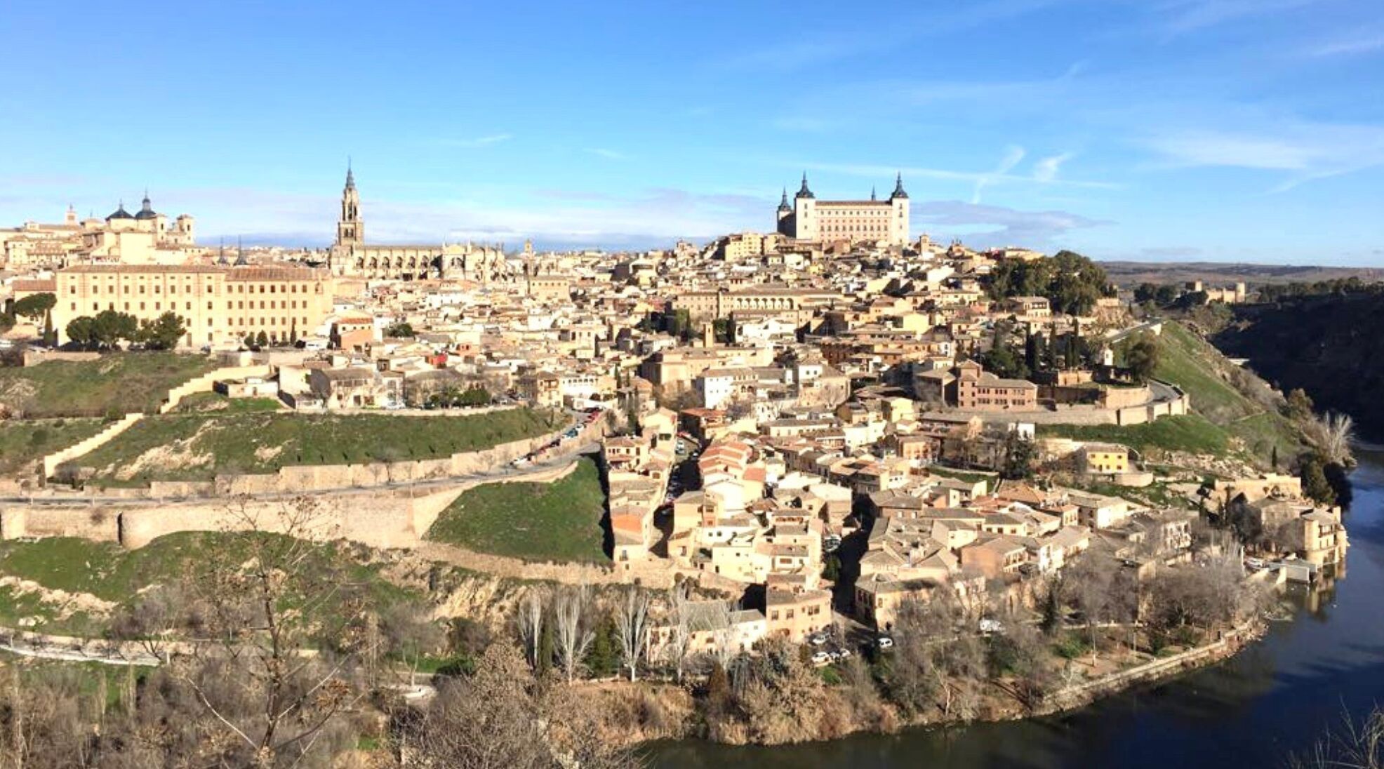 Un pueblo histórico con un castillo destacado en una colina, rodeado por una muralla y un río.