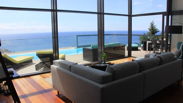 A modern living room with a large window overlooking a pool and the ocean. - Sea House Madeira - Atlantic Ocean (garajau)